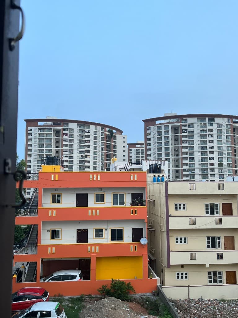 An orange apartment building in Bengaluru with cream neighbors and modern high-rises in the distance.